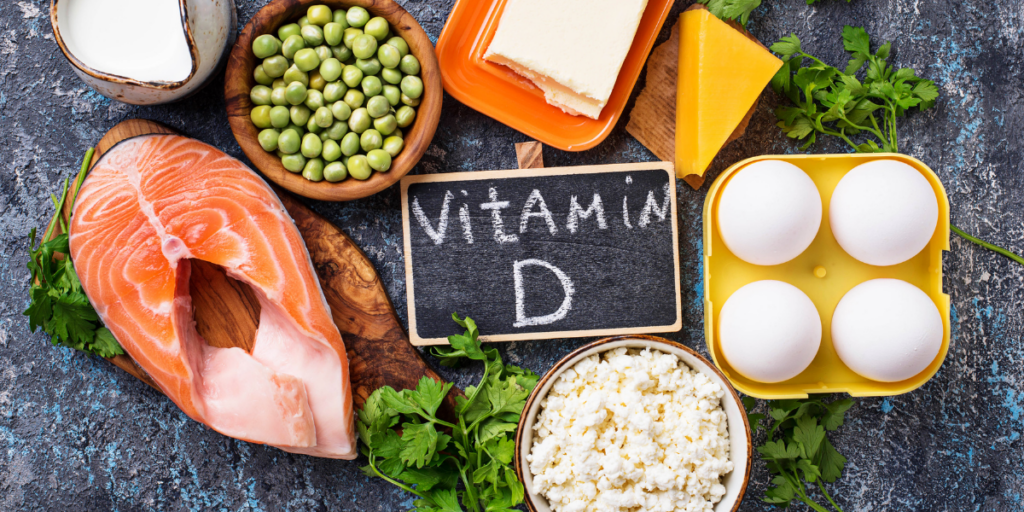 D vitamini içeren besinler (bezelye, süt, peynir, yumurta, balık) ve ortasında vitamin D yazan bir tahta
